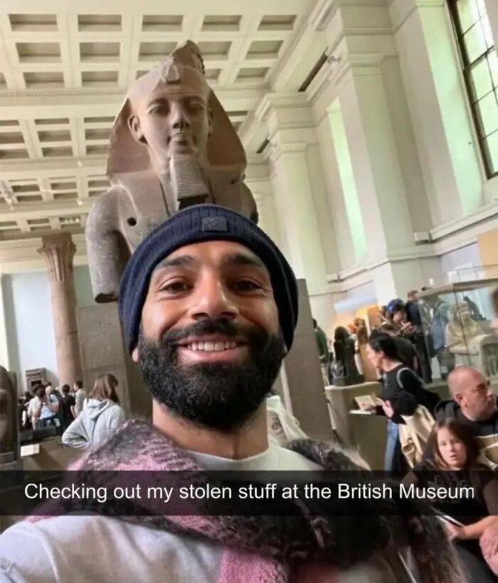A man smiling and taking a selfie in front of an ancient Egyptian statue at the British Museum, with a caption about his 'stolen stuff', shared as a No Context Humans meme.