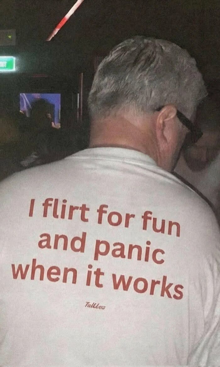 A man from behind wears a white T-shirt with the phrase 'I flirt for fun and panic when it works,' providing entertaining memes for X.