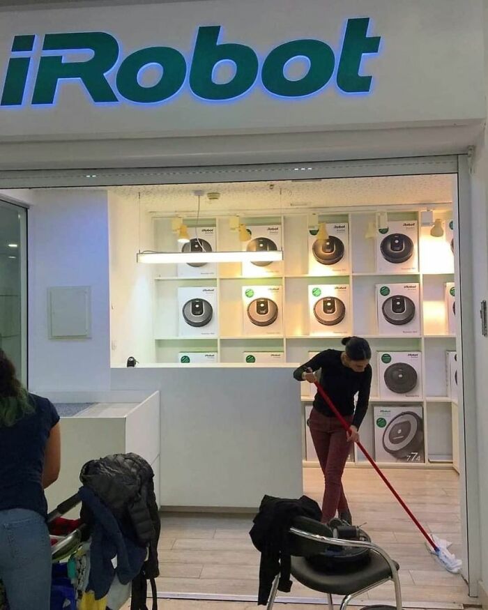 A person mopping the floor in front of an iRobot store, which is full of robot vacuum cleaners. This image is one of the entertaining memes shared on No Context Humans.