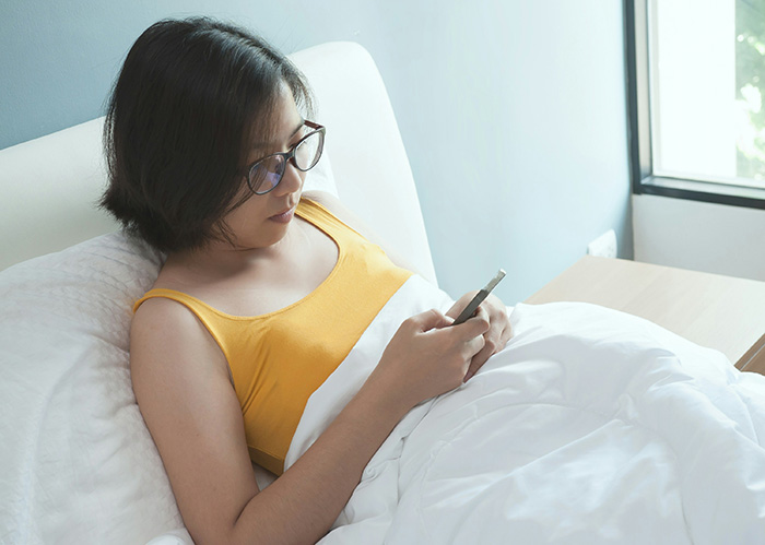 A woman in bed looks at her phone, dealing with her husband's old pics with his ex. A woman in bed looks at her phone, dealing with her husband's old pics with his ex.