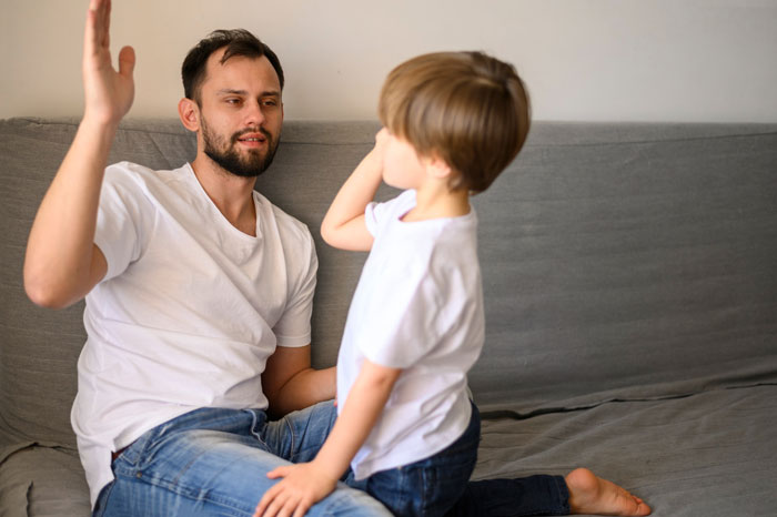 A man with a beard and a young child in white t-shirts, engaged in a conversation on a couch. A man with a beard and a young child in white t-shirts, engaged in a conversation on a couch.