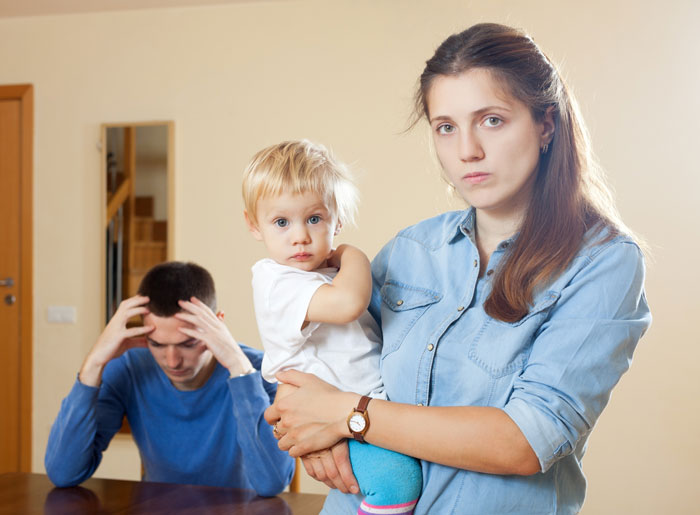 A worried pregnant wife holding her 4YO, while the husband sits with his head in his hands, after he cheats on pregnant wife. A worried pregnant wife holding her 4YO, while the husband sits with his head in his hands, after he cheats on pregnant wife.