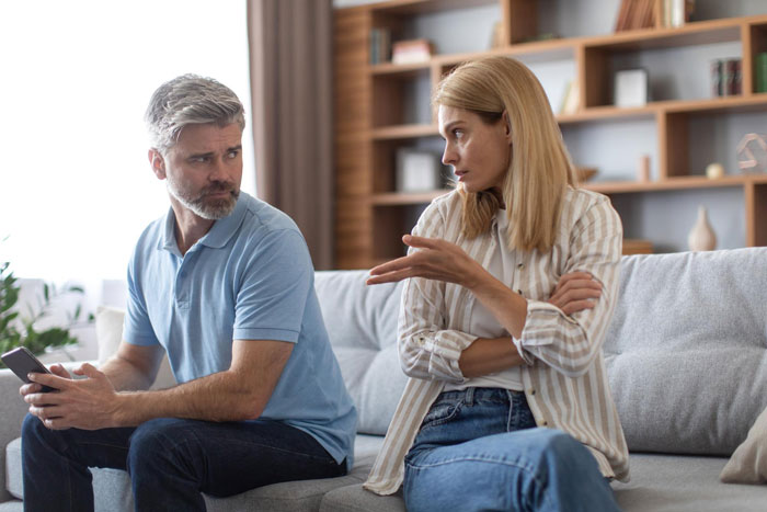 A couple arguing on a couch. The man looks away from the woman. The woman has her arms crossed, looking at the man. A couple arguing on a couch. The man looks away from the woman. The woman has her arms crossed, looking at the man.