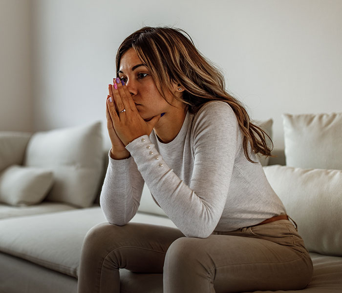 A woman looking distressed on a couch, seeking advice as she finds out her husband is not who she thought.