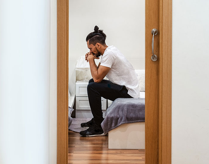 A man sitting on the bed, looking distressed, as a woman finds out who her husband really is.