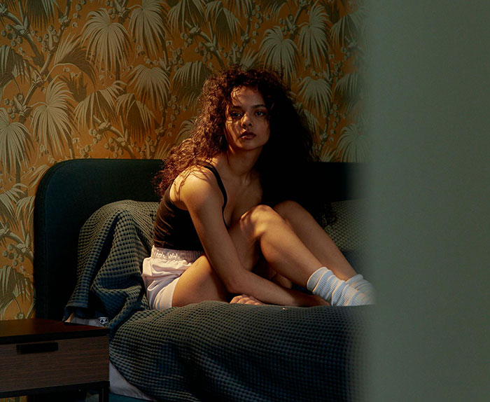 A pensive woman sits on the edge of her bed, reflecting on the shocking discovery that she has no idea who her husband really is.