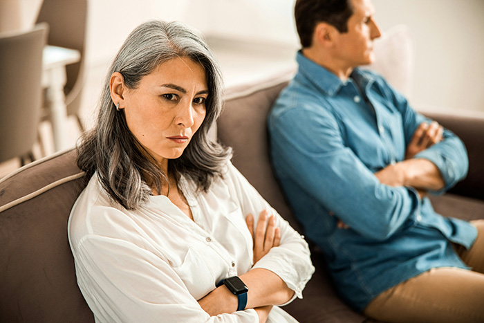Man with shiny spine kicks mom out of home. Woman with gray hair sits with crossed arms, looking displeased. Man with shiny spine kicks mom out of home. Woman with gray hair sits with crossed arms, looking displeased.