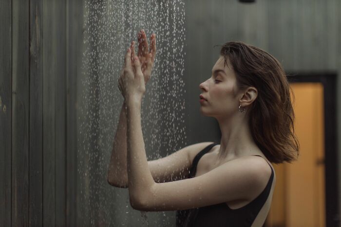 A woman under a shower, eyes closed, hands raised, feeling the water. This serene moment contrasts with the pure chaos of identical twin life.