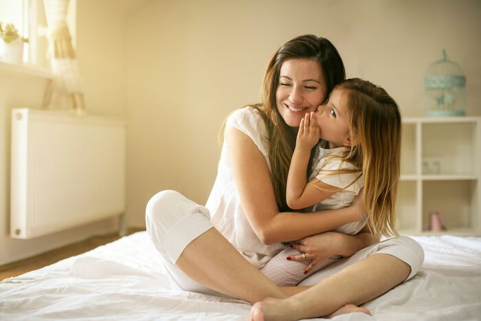 A mother and her identical twin daughter, sharing a sweet moment of affection on a bed, avoiding pure chaos.