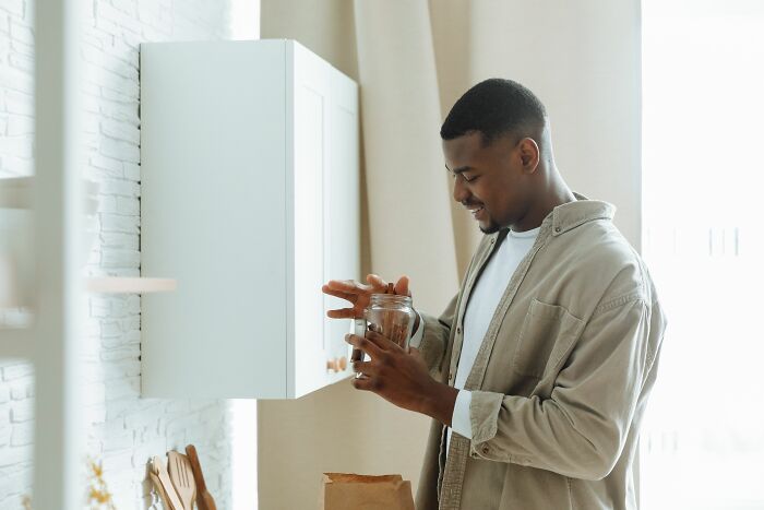 A man smiles, holding a jar in his kitchen, a moment of calm in an identical twin's busy life.