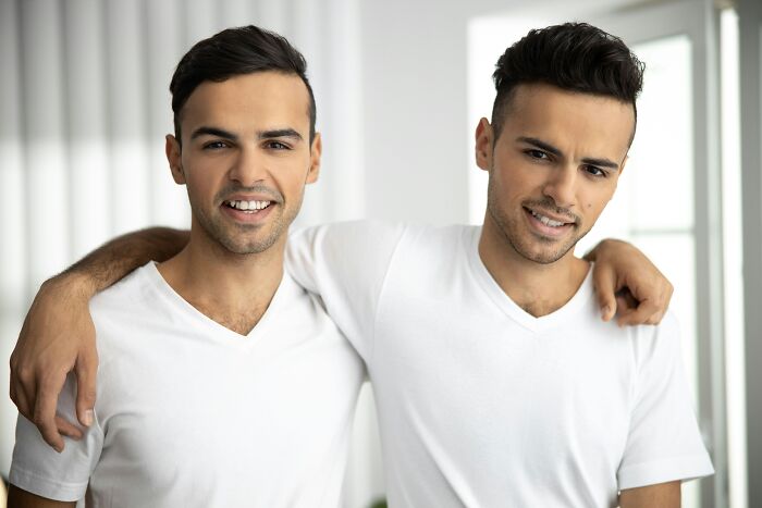 Identical twin brothers smiling and posing with an arm around each other, showcasing their pure chaos.