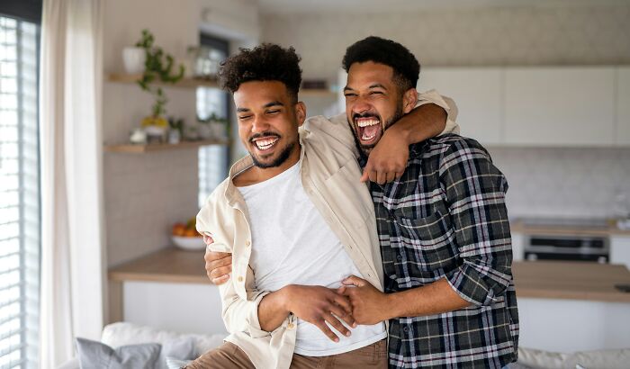 Two happy identical twin brothers laughing and embracing each other in a modern living room.