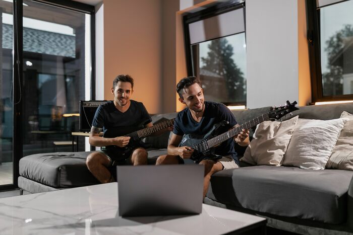 Identical twin brothers playing electric guitars together while looking at a laptop, sharing a moment of pure chaos.