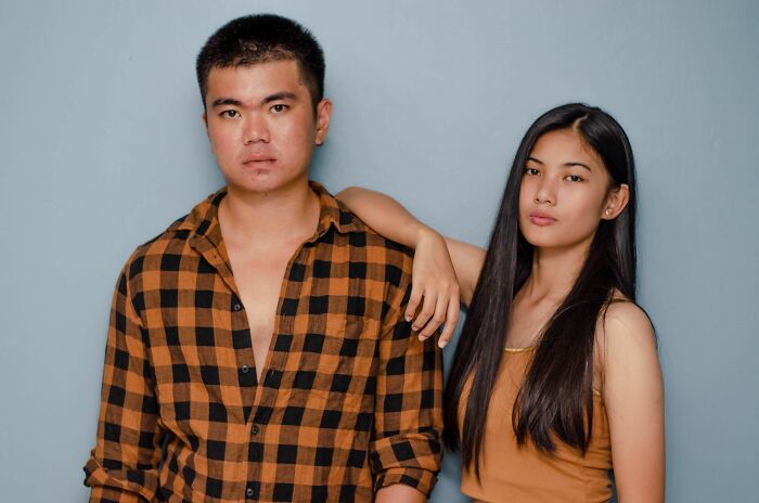 A serious looking identical twin brother and sister posing against a light blue wall.