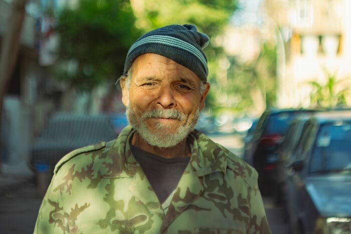 An older man with a grey beard and a beanie, smiling. His expression hints at life's pure chaos, possibly from an identical twin.