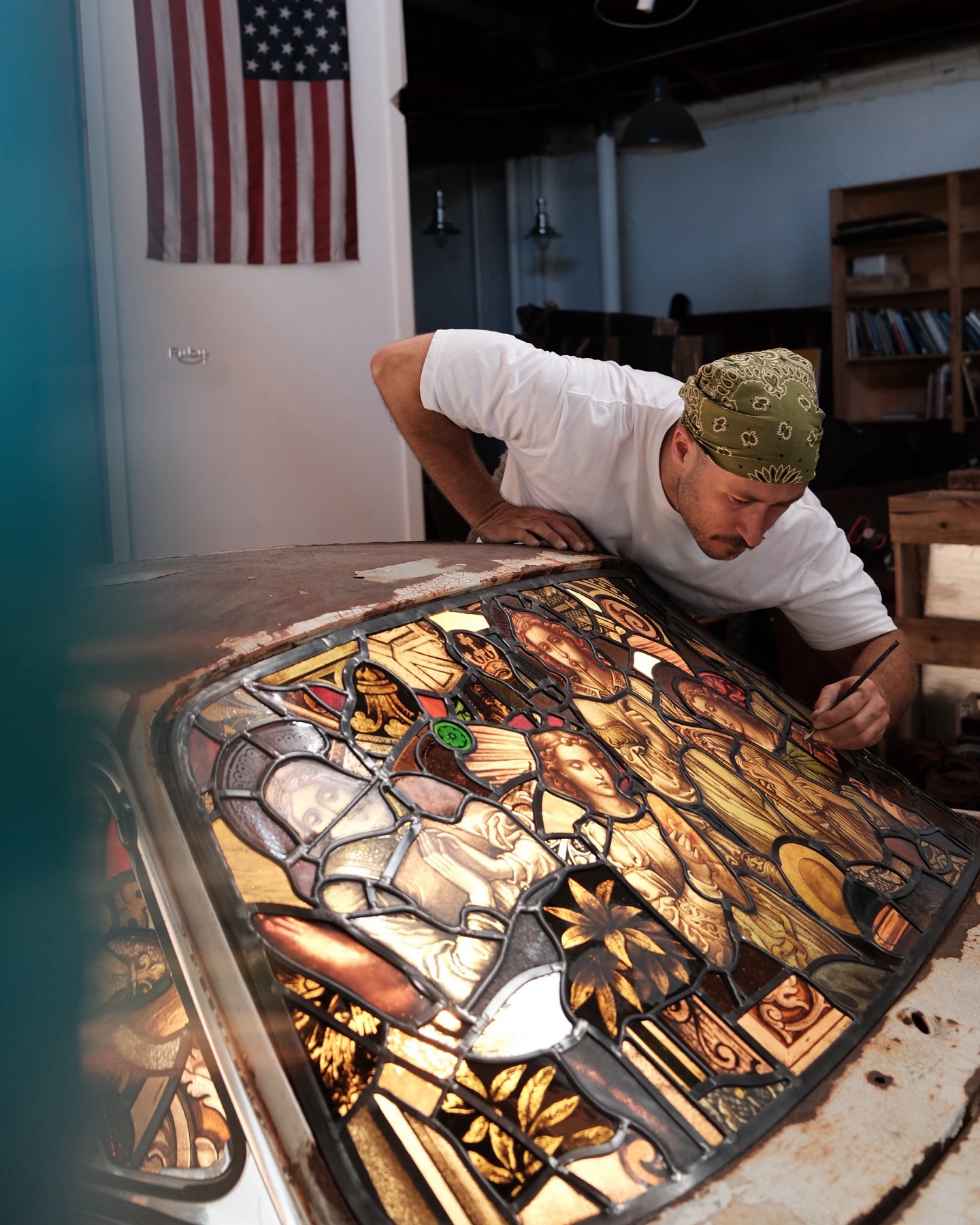 Artist meticulously working on a stained-glass sculpture, integrating it into a burned and rusted Porsche 911.