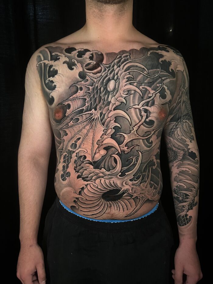 A professional tattoo artist's work: a detailed dragon and wave chest and arm tattoo design on a man.