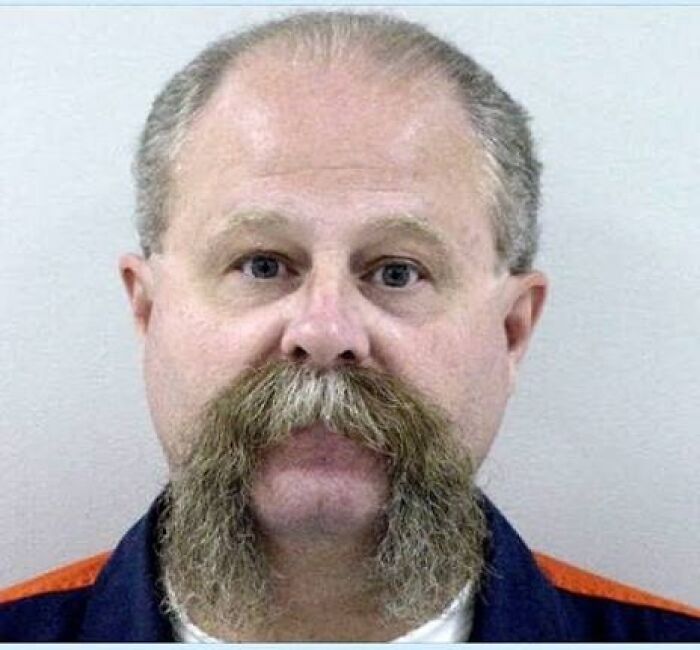 A terrifying mugshot of a man with a large mustache and a serious expression, embodying a 'We Need To Leave Now' moment.