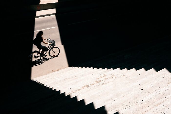 A perfectly timed street photo of a cyclist riding through a stark contrast of light and shadow, revealing extraordinary moments.