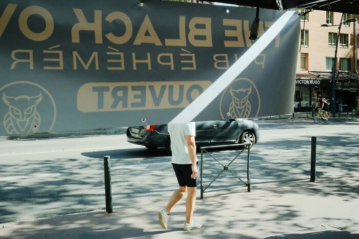A perfectly timed street photo of a person walking under a banner, with a light beam across the banner, revealing extraordinary moments.