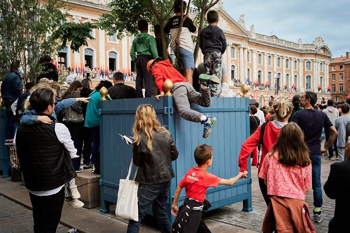 A perfectly timed street photo of children climbing on a blue barrier in a crowd, revealing extraordinary moments.