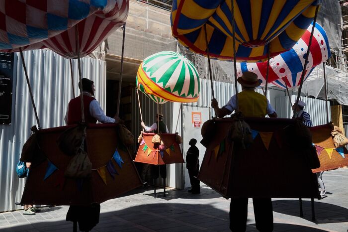 A perfectly timed street photo of performers in hot air balloon costumes on a sunny street, revealing extraordinary moments.