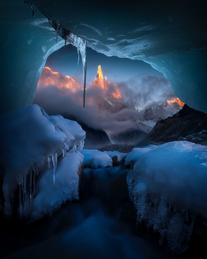 Remarkable color photo of a vibrant icy cave opening to mountains at sunset.