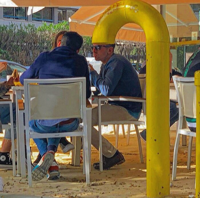 Photographer captures perfectly timed coincidences of a man sitting under a curved yellow pipe in Barcelona.