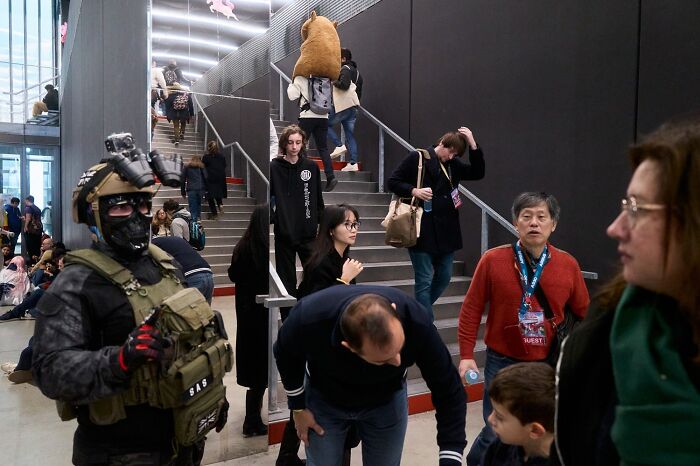 A perfectly timed street photo captures a person in tactical gear amidst a bustling crowd ascending stairs.