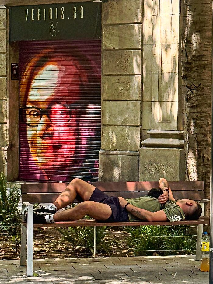 Photographer captures perfectly timed coincidences of a man sleeping on a bench next to a mural in Barcelona.