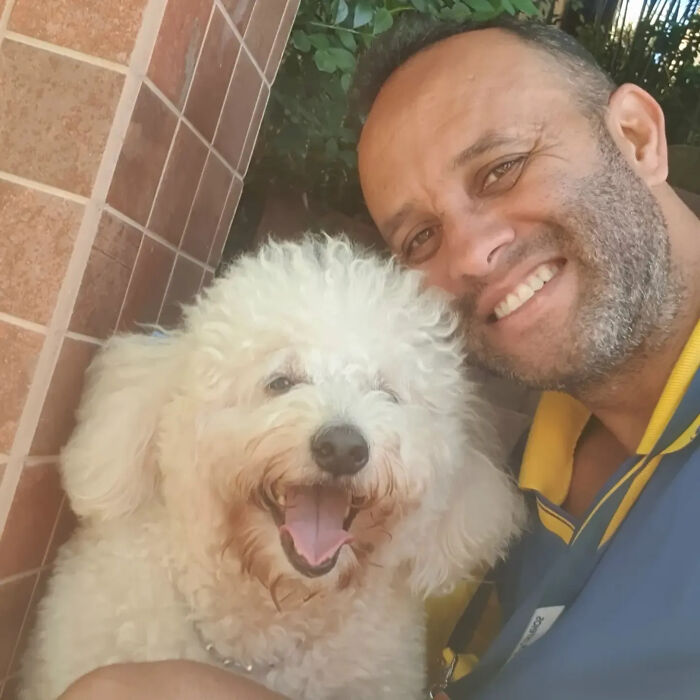 A mailman smiles with a fluffy white dog, capturing a heartwarming moment during his deliveries.