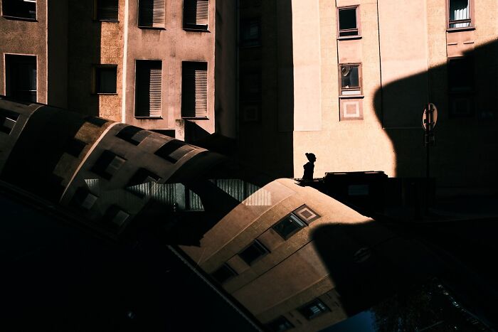 A perfectly timed street photo reveals a silhouette of a person on a rooftop with reflections on a car windshield.