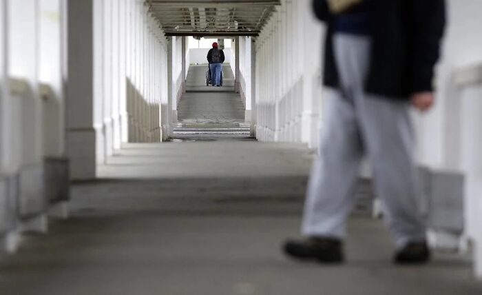 A person in a long hallway, walking away, with another person in the distance, representing wholesome people helping each other.