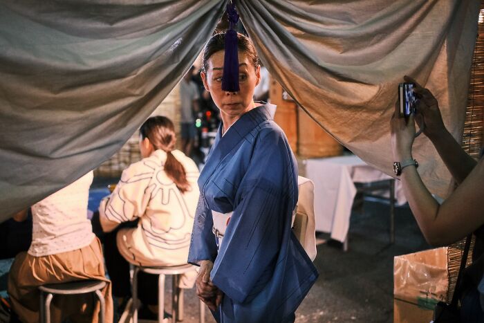 An extraordinary street photo captures a woman in a blue kimono under a draped fabric, looking over her shoulder.