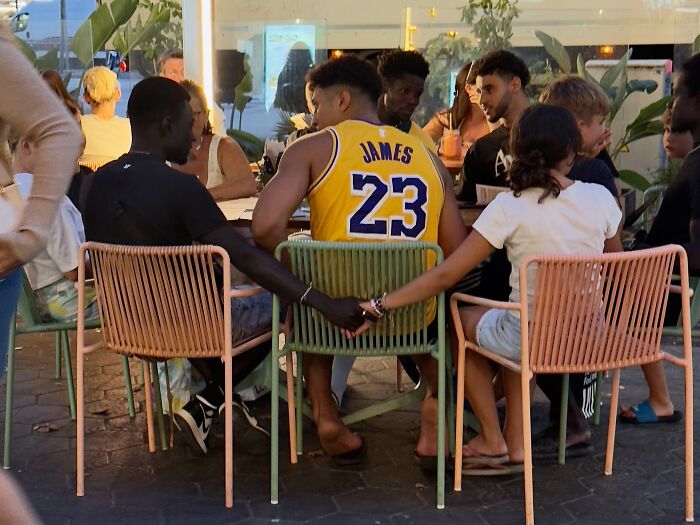 People seated around tables, with a couple holding hands discreetly, showing perfectly timed coincidences on Barcelona streets.