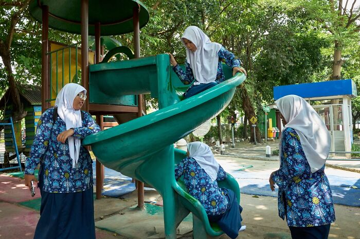 Three women on a playground slide, a perfectly timed street photo revealing extraordinary moments in everyday life.