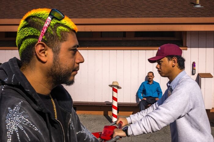 A photographer captures humor and chaos of two men facing each other, with a third man in the background in everyday life.