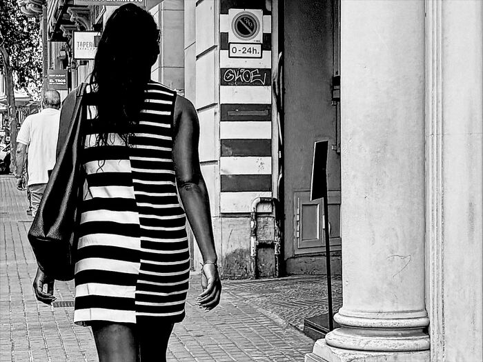 A woman in a black and white striped dress walks past a striped pole, creating a perfectly timed coincidence in Barcelona.