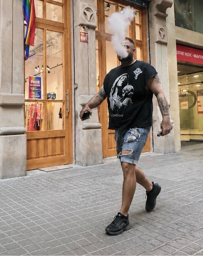 A man exhaling a cloud of vape smoke, resembling an explosion, captured as a perfectly timed coincidence in Barcelona.