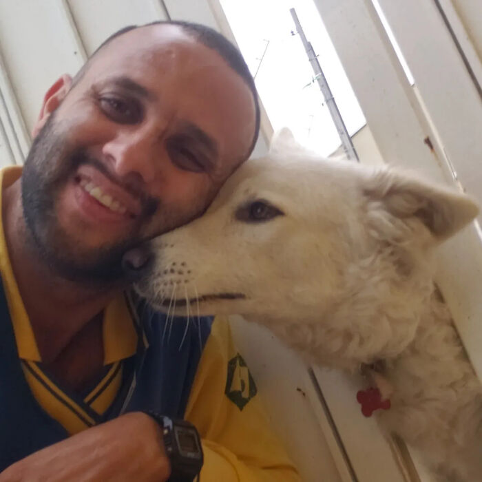 A mailman smiles, taking a selfie while embracing a white dog, showcasing their special bond during deliveries.