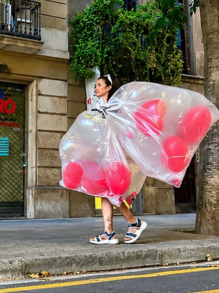A woman carrying large clear bags filled with pink balloons walks down a street in Barcelona, a perfectly timed coincidence.
