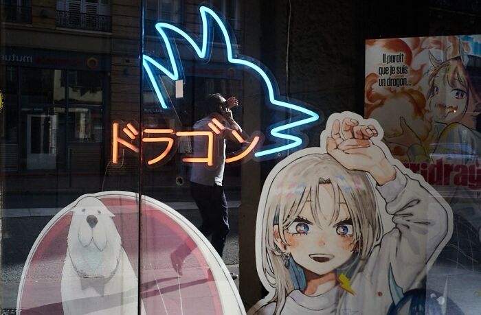 A street photo of a person silhouetted by a neon dragon sign, capturing extraordinary moments in everyday life.