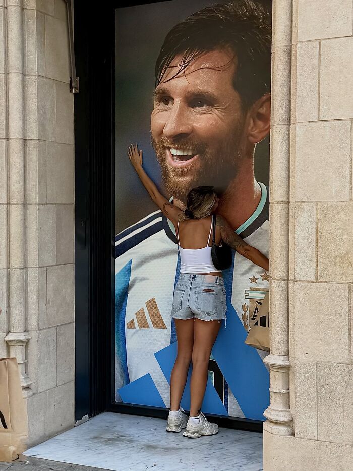 Photographer captures perfectly timed coincidences: a woman hugging a giant Messi poster on the streets of Barcelona.