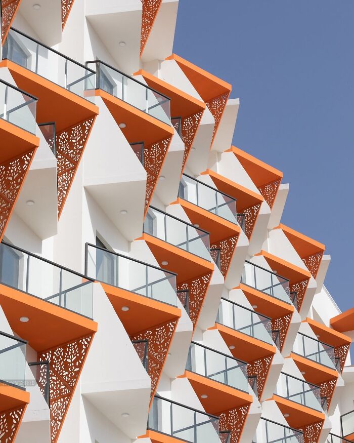 A modern building facade showcases brilliant design choices with repeating orange, triangular balconies.