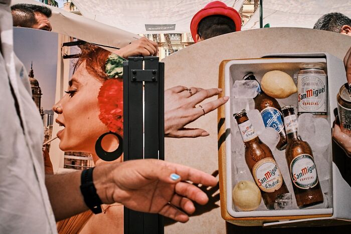 A perfectly timed street photo creates a collage of hands, a woman's profile, and a cooler with San Miguel beer.