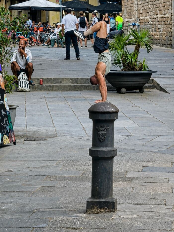 A photographer captures perfectly timed coincidences in Barcelona: a man doing a handstand on a bollard.