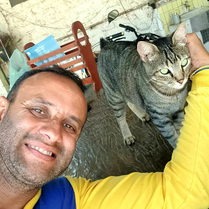 A mailman takes a selfie with a tabby cat, demonstrating his affectionate interactions with animals on his route.