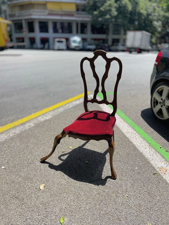 A vintage red velvet chair sits abandoned on a street in Barcelona, a perfectly timed coincidence of unexpected placement.