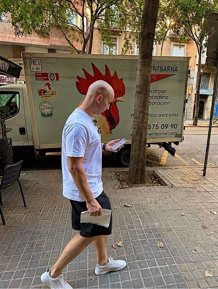A photographer captures perfectly timed coincidences with a man walking past a truck with a rooster head in Barcelona.