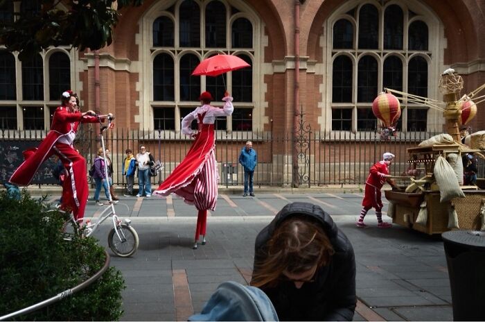 Street performers on stilts and a unicycle entertain a crowd, a perfectly timed street photo of extraordinary moments.